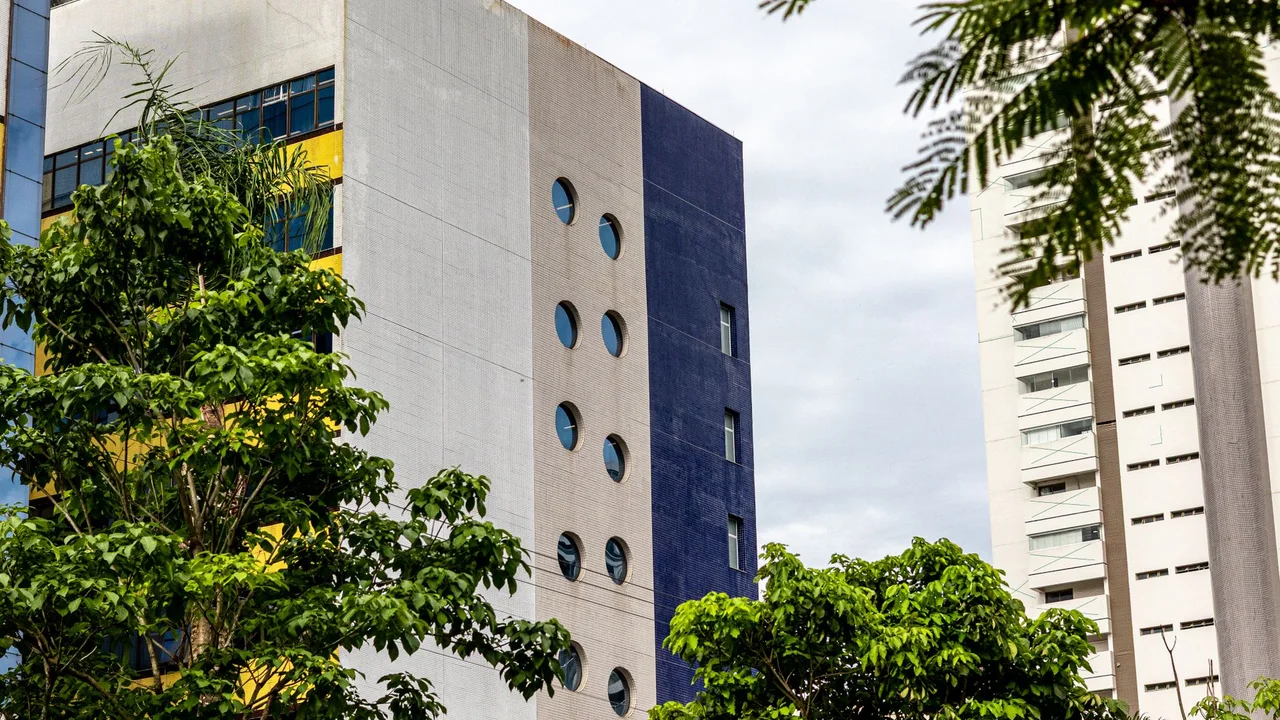 A contemporary building façade with circular windows surrounded by lush greenery in an urban setting.