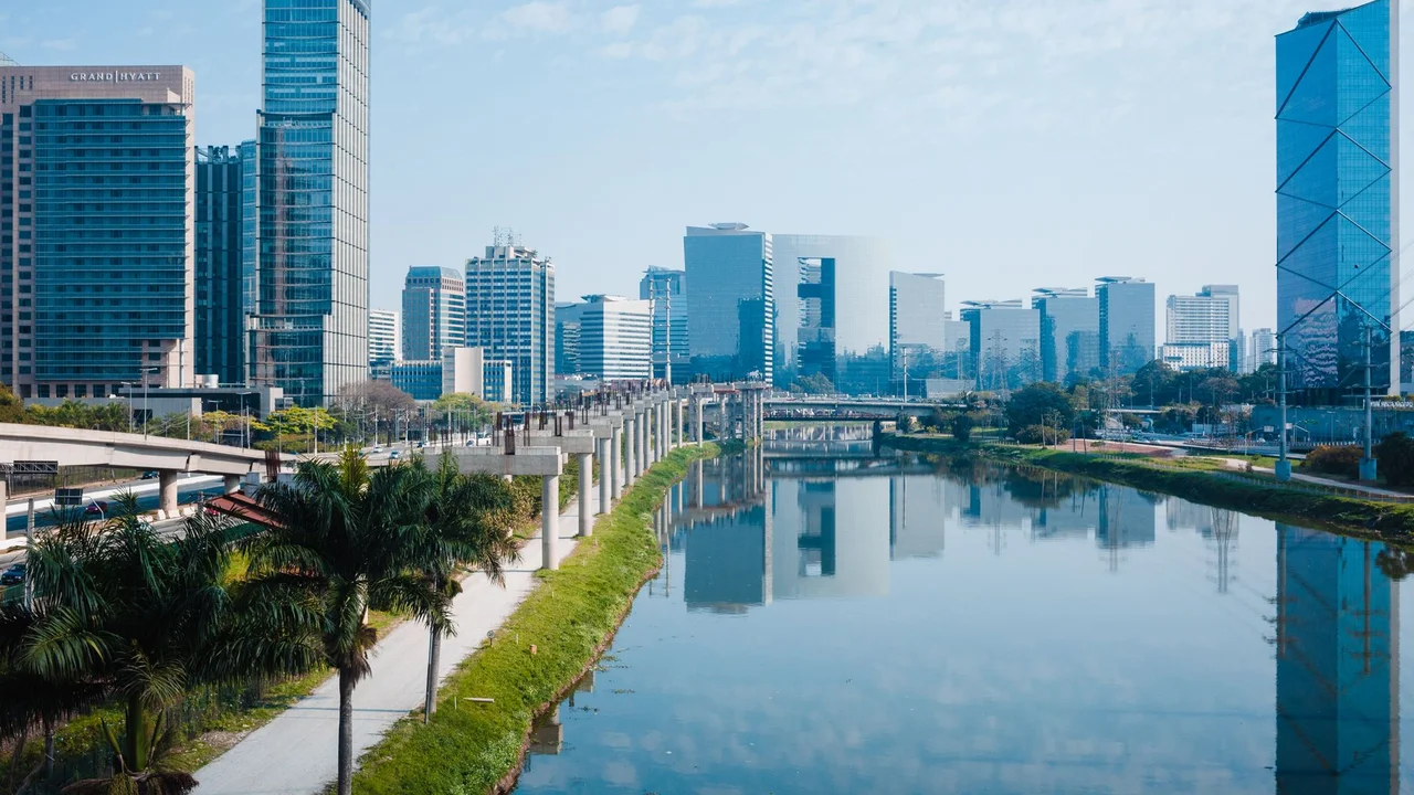 Stunning view of a modern city skyline reflecting in the river with clear blue sky.
