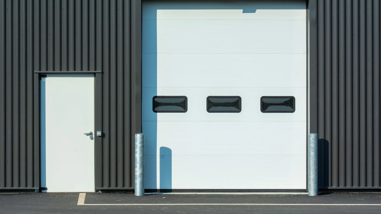 A modern industrial warehouse facade with a large white garage door and side entrance.