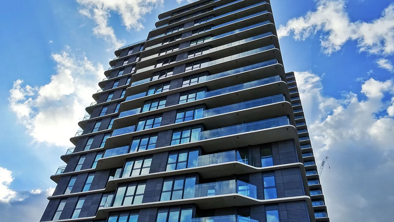 A contemporary skyscraper with glass windows and balconies under a partly cloudy sky.