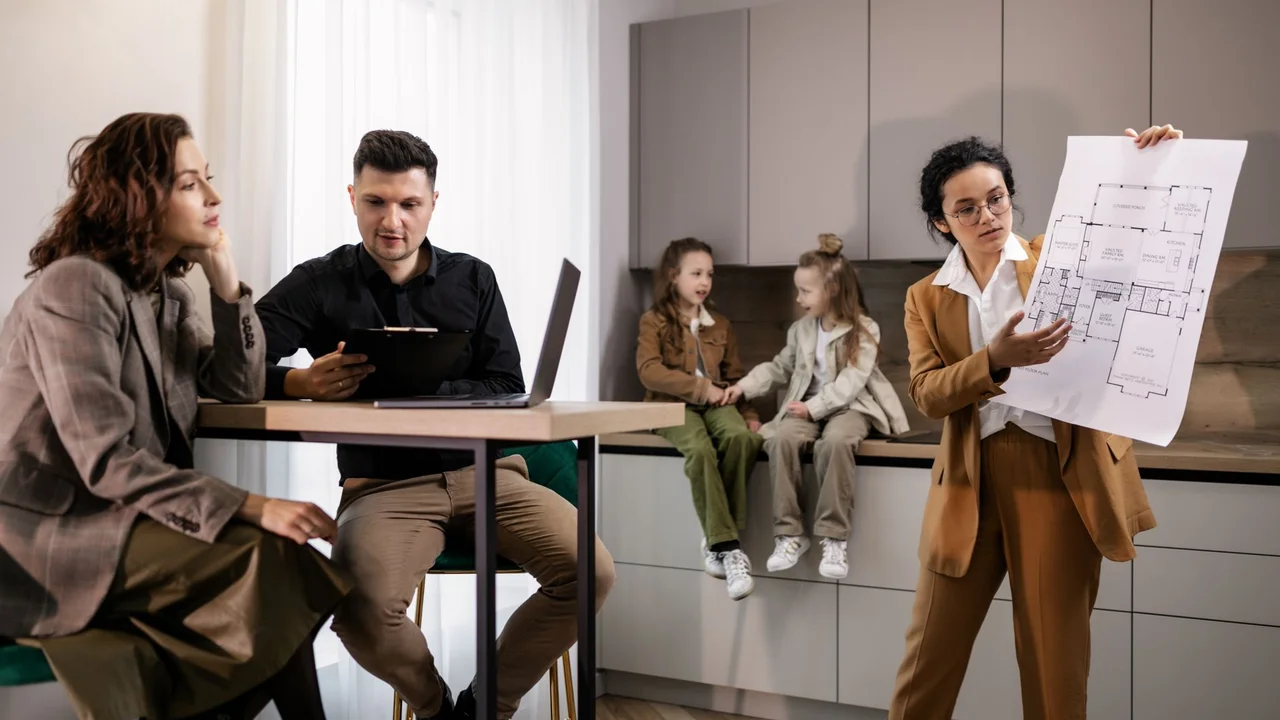 Real estate agent presenting house plans to clients in a modern kitchen setting.