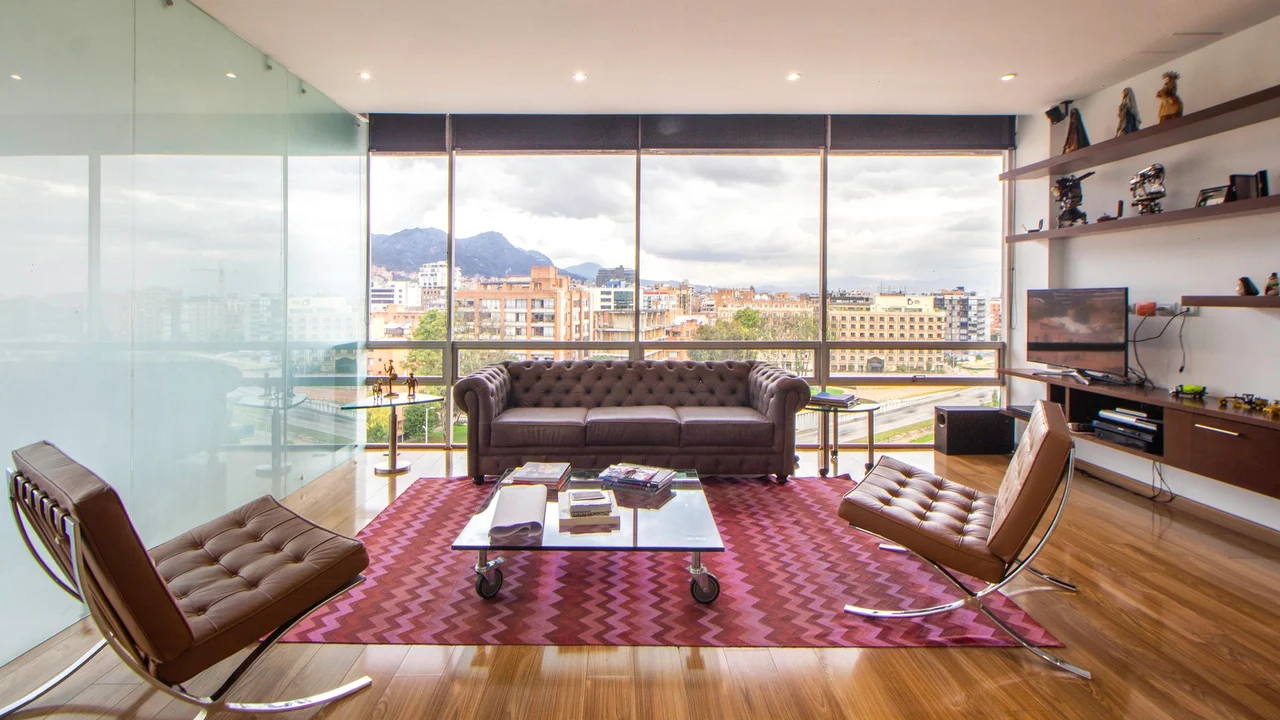 A stylish, minimalist living room featuring large windows, modern furniture, and a cityscape view.