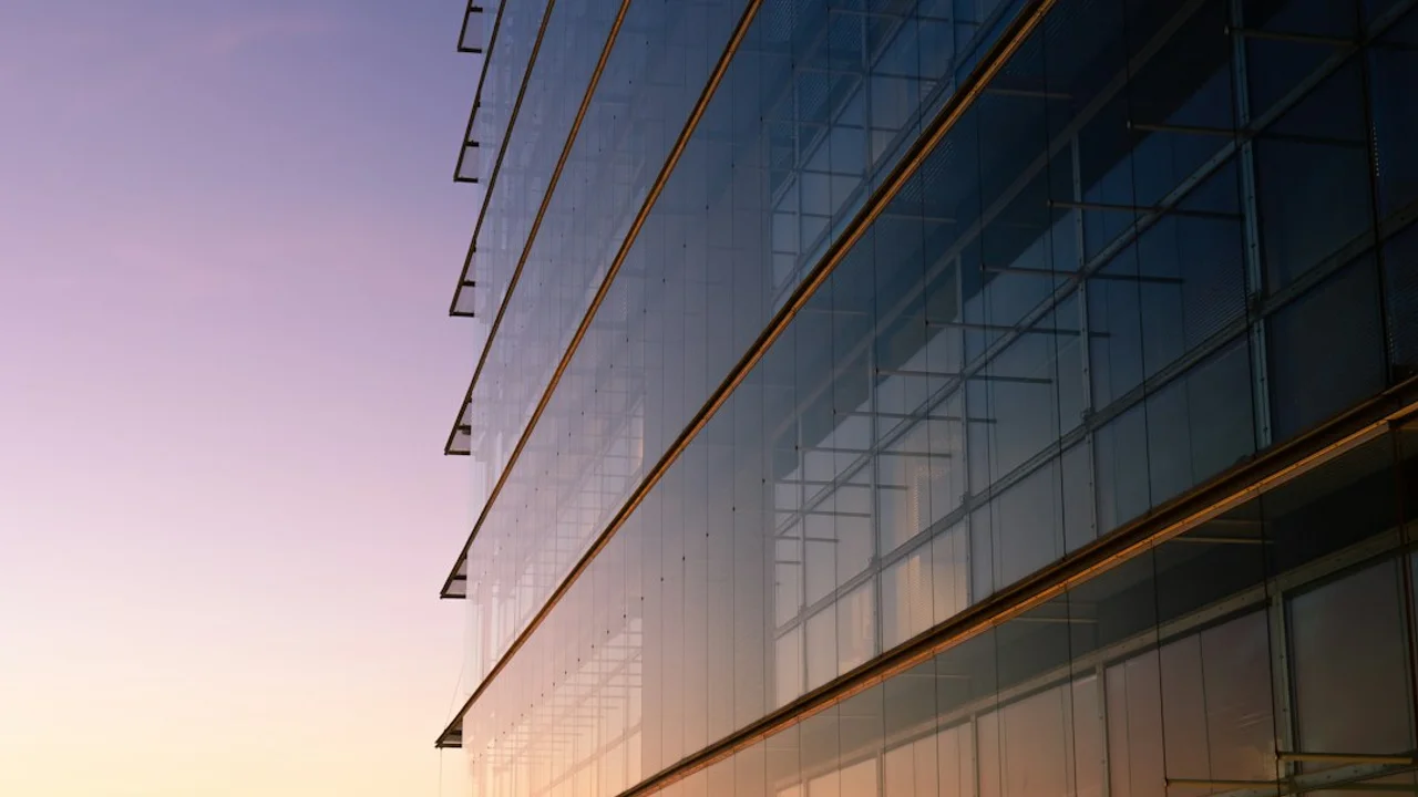 A modern glass office building facade reflecting a soft purple and orange sky