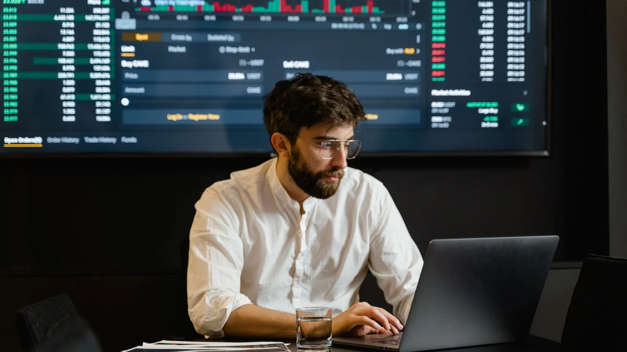 Professional analyzing stock market trends using laptop and digital display in modern office.