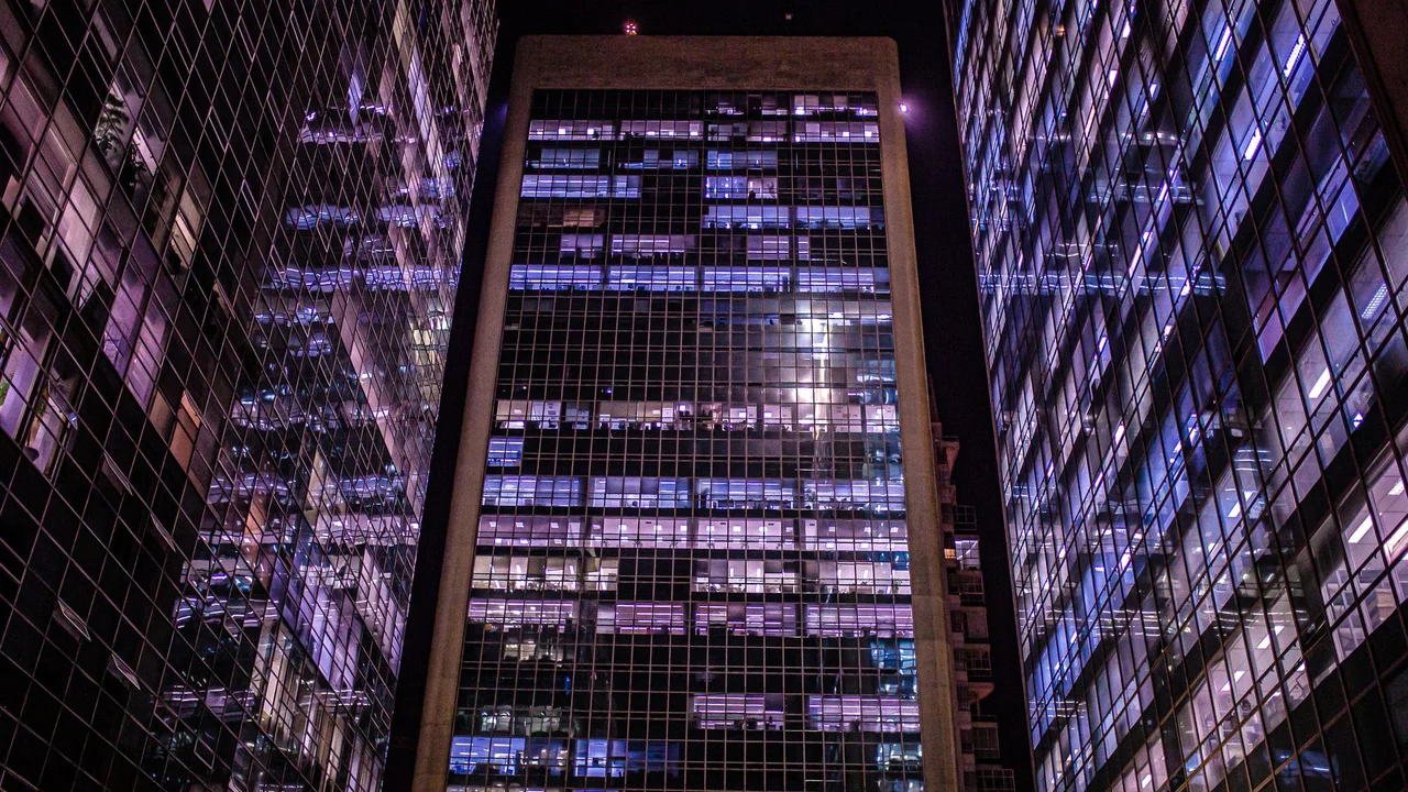 A low angle shot of illuminated modern skyscrapers with glass facades at night, reflecting urban architecture.