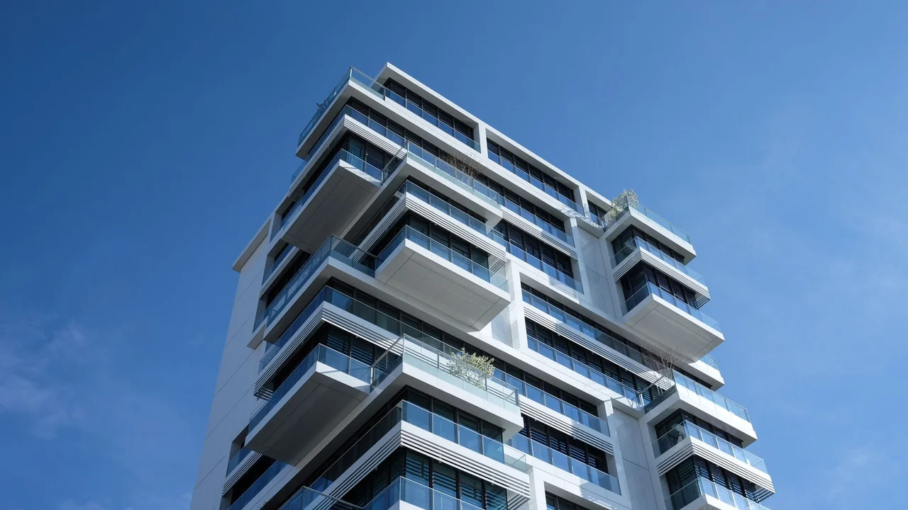 Striking low-angle shot of a modern condominium with unique balcony design and clear blue sky.